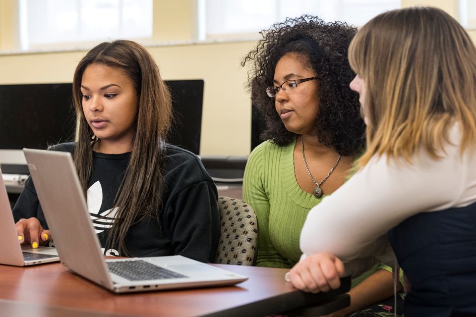 Three students looking at two laptops conversing 