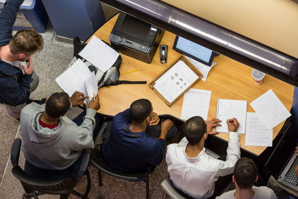 Four Students studying around a desk with papers on it